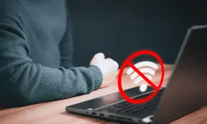 Laptop nie widzi wifi. Czerwony okrąg z przekreślonym symbolem wifi nad klawiaturą sugeruje problem z połączeniem internetowym.
