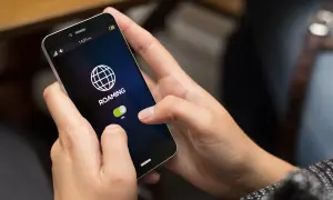 Dłoń dotyka ekranu smartfona, pokazując opcję "ROAMING" z przełącznikiem w pozycji "ON". Dowiedz się, jak wyłączyć roaming w telefonie, aby uniknąć dodatkowych kosztów.