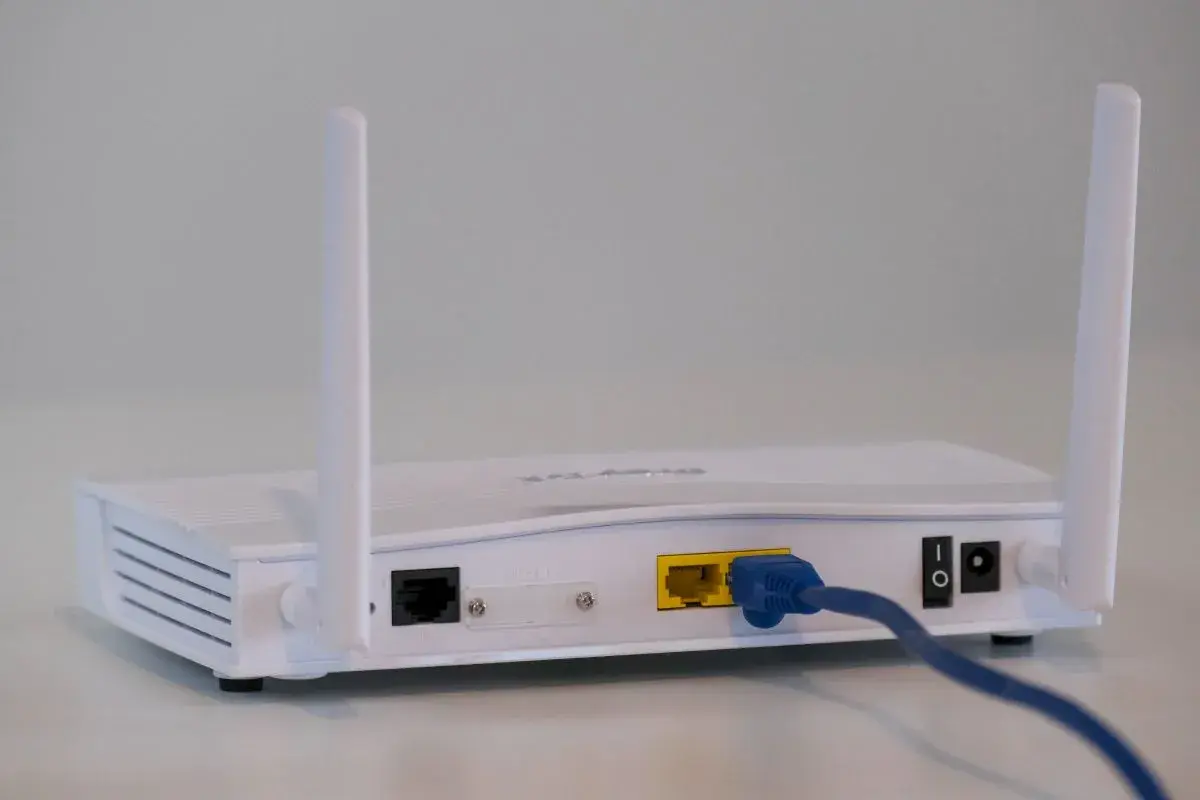 Biały modem a router z dwoma antenkami, podłączony niebieskim kablem Ethernet.