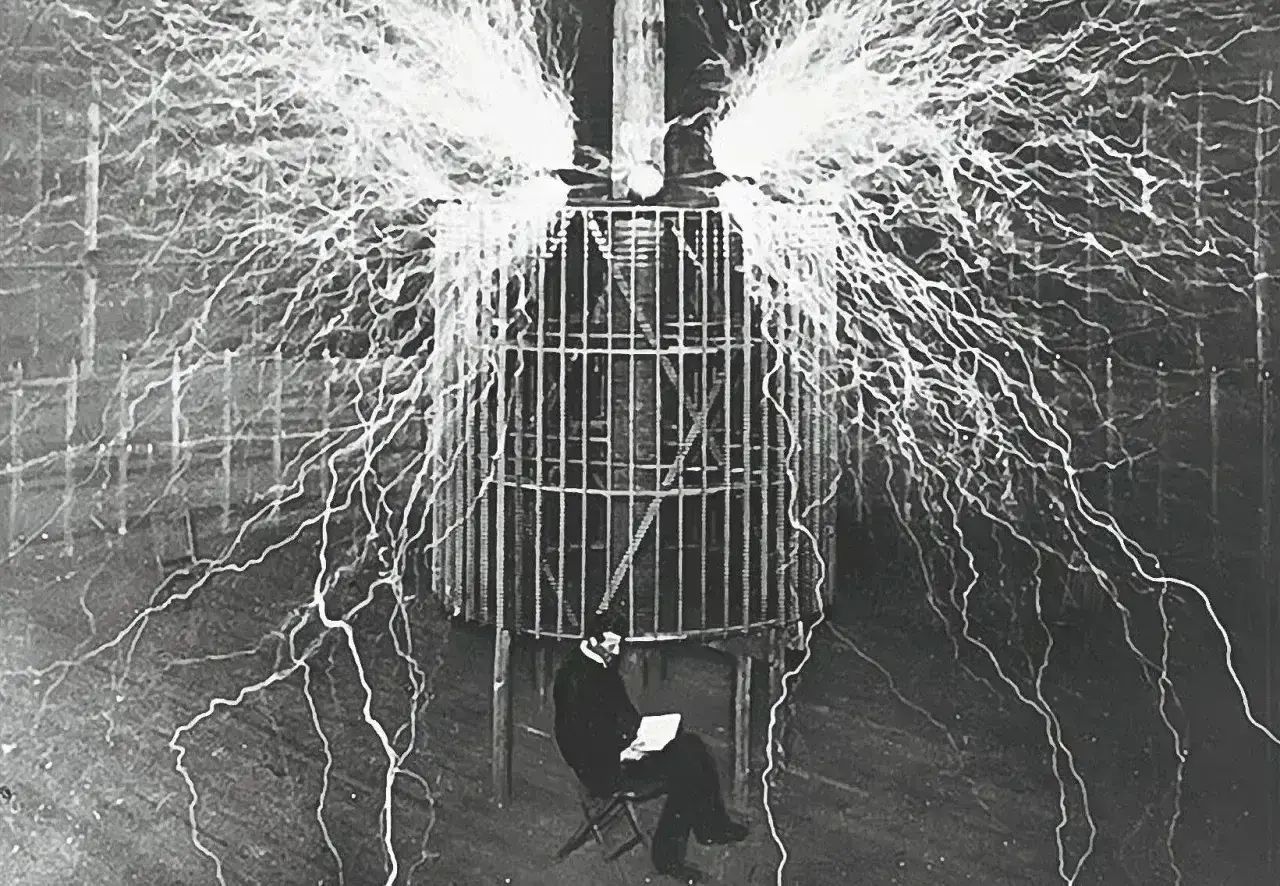 Nikola Tesla, który udowodnił, kto wynalazł prąd, siedzi bezpiecznie w klatce podczas eksperymentu z wyładowaniami elektrycznymi.