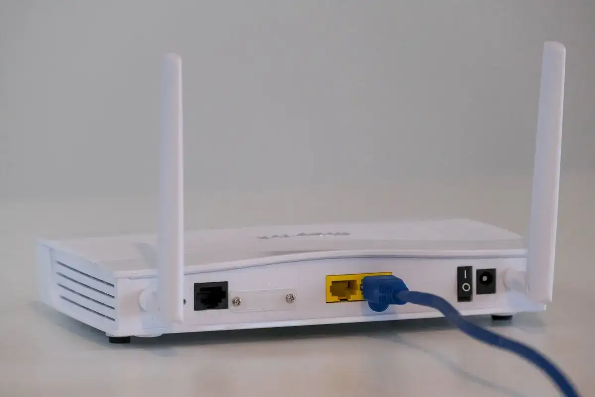 Biały modem a router z dwoma antenkami, podłączony niebieskim kablem Ethernet.