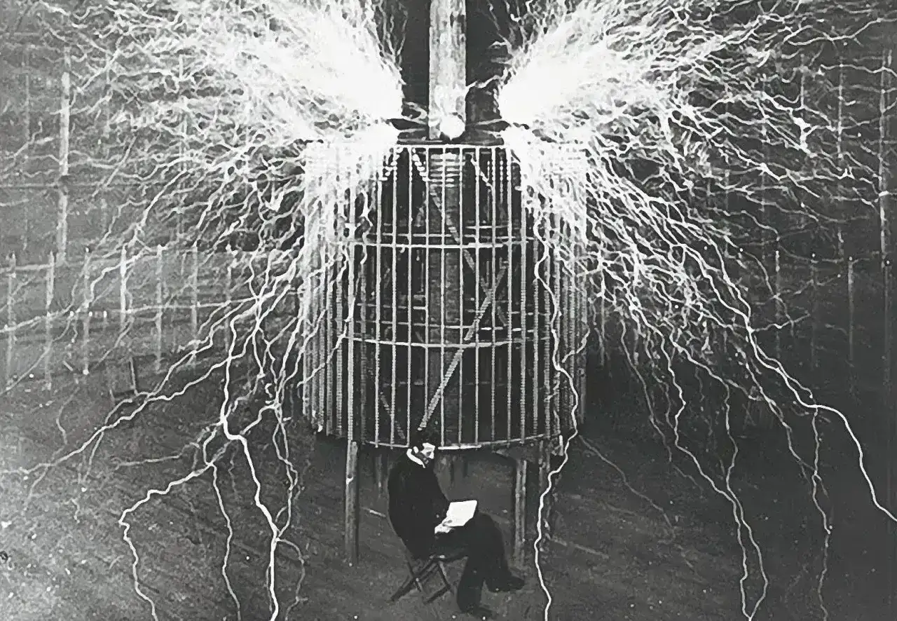 Nikola Tesla, który udowodnił, kto wynalazł prąd, siedzi bezpiecznie w klatce podczas eksperymentu z wyładowaniami elektrycznymi.
