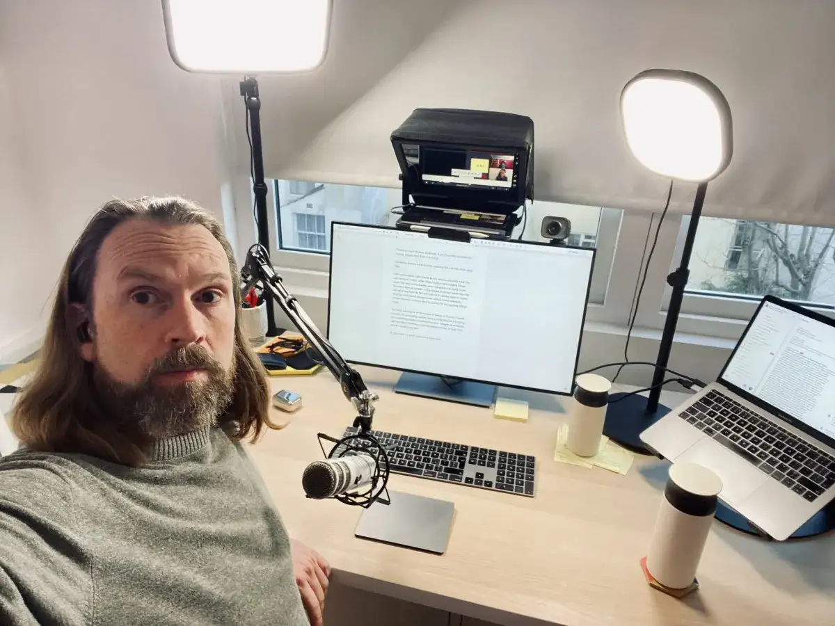 Mężczyzna z brodą i długimi włosami siedzi przy biurku, gotowy do rozmowy przez Skype. Na ekranie komputera widać okna rozmowy.