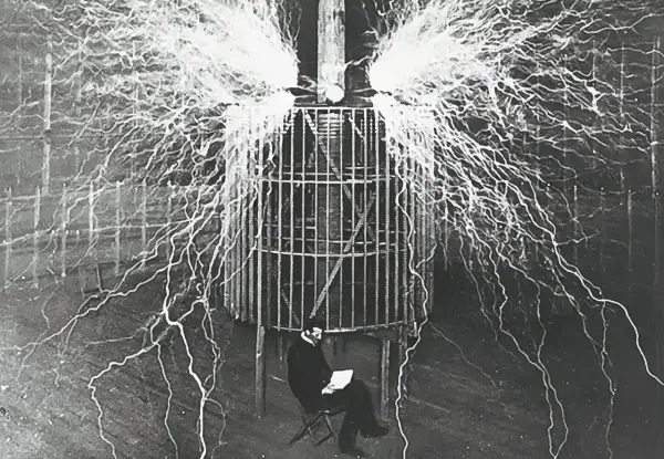 Nikola Tesla, który udowodnił, kto wynalazł prąd, siedzi bezpiecznie w klatce podczas eksperymentu z wyładowaniami elektrycznymi.