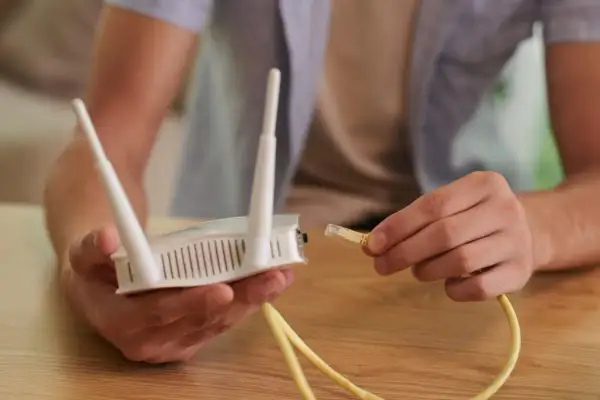 Mężczyzna podłącza kabel Ethernet do routera, pokazując, jak podłączyć wzmacniacz wifi.