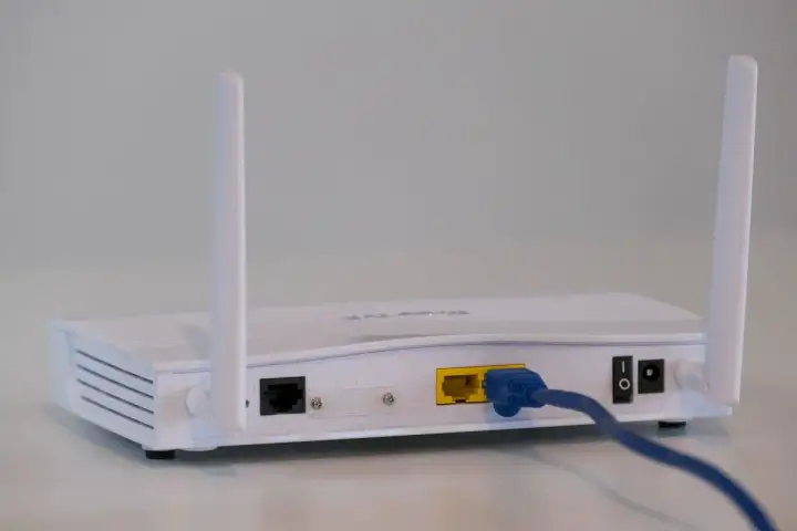 Biały modem a router z dwoma antenkami, podłączony niebieskim kablem Ethernet.